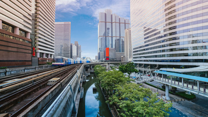Skytrain among the skyscrapers. Water canal and trees. Urban life and nature