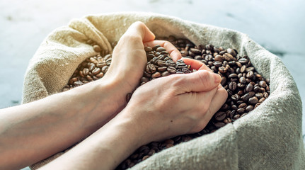 Hands hold a handful of heart-shaped roasted coffee beans over a full burlap of coffee. Сoncept of love for coffee