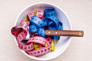 Many colorful measuring tapes in bowl on table