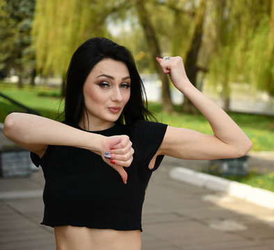 Fitness model posing against the backdrop of a city park in fine weather. Photo in spring weather outdoors, a brunette girl with a slender figure shows biceps arms.