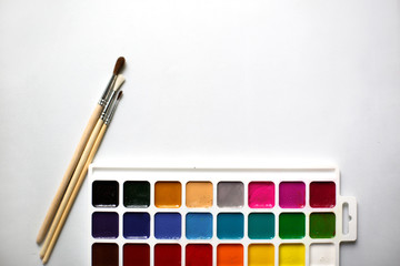 A palette of eighteen-color watercolors and paintbrushes on a white background with space for text.