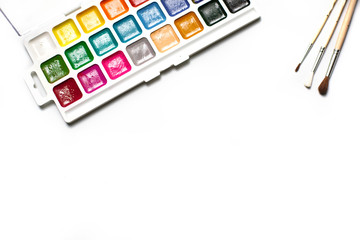 A palette of eighteen-color watercolors and paintbrushes on a white background with space for text.