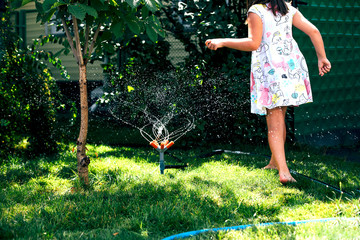 Child playing with garden sprinkler. Happy Girl in dress running and jumping. Kids gardening....