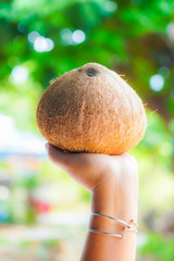 The coconut is in the beautiful hands of the woman lifting up.