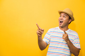 Young happy&funny asian man pointing finger on blank space for text on yellow background.