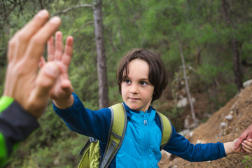 A boy with a backpack climbed to the top of the mountain and gives five.