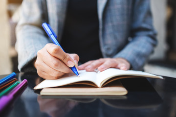 Closeup image of a woman writing on a blank notebook with colored pens on the table