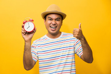 Young asian man holding the alarm clock on yellow isolated background.