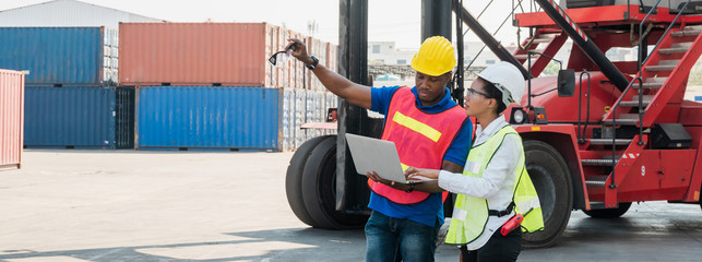 Two Black foreman man & woman worker working checking at Container cargo harbor holding laptop...