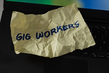 crumpled piece of paper with the hand-written "Gig Workers" lying on the computer keyboard.  The concept of short-term contracts for work and poor employee protection