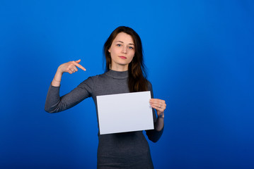 Young woman in grey shirt holding a sheet of paper and looking at the camera, smiling. Blue background isolated