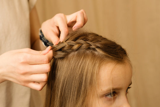 Process of braiding the master weaves braids on her head blond little girl in beauty salon close up. Professional hair care and creating hairstyles.