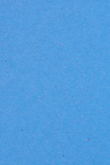 The surface of a sheet of blue or azure cardboard. Rough natural paper texture with cellulose fibers. Bright saturated color. Background or wallpaper. View from above. Vertical shot. Macro