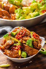 Portrait of a teriyaki chicken bowl sprinkled with seesame seeds, fresh chillies and broccoli with more food in a bowl in the back