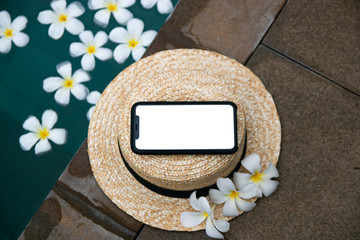 Smartphone screen in the tropics on a straw hat surrounded by beautiful flowers