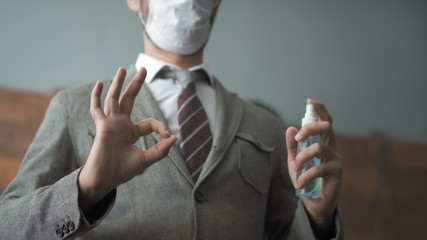 Businessman shows ok gesture holding a sanitizer or antiseptic liquid. Close up shot. Positive man in a protective mask works in the office during an outbreak of coronavirus