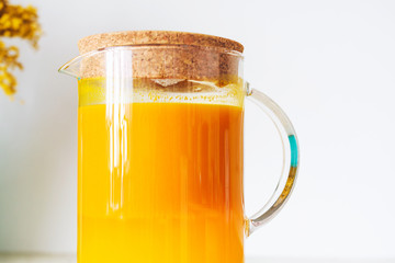Jug with sea buckthorn juice on a white background. Close-up.
