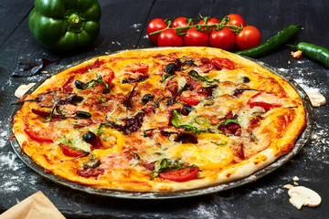 Pizza with mozzarella cheese, tomatoes, mushrooms, peppers, herbs on a dark wooden background.