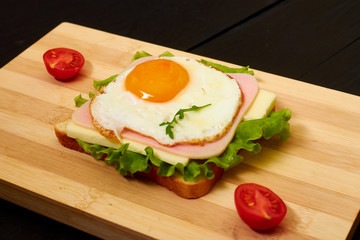 Toast with ham, egg and tomato on a light wooden board.