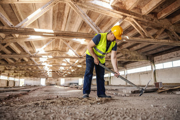 Full length of construction site builder using pickax on site.