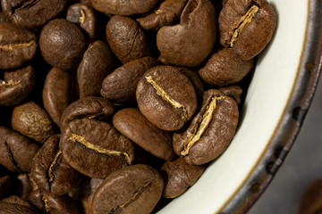 A top down macro closeup view of medium roasted coffee beans in a cup.