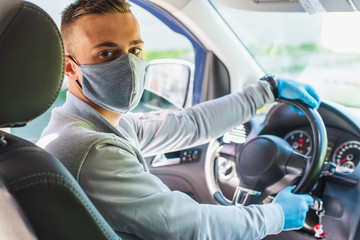 Quarantine concept. Pandemic. A young guy-taxi driver in a gray protective medical mask and a gray jacket is sitting behind the driver's seat in the car. He looks straight. Virus. Coronavirus.