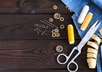sewing tools and materials scissors thread needles buttons lie on a dark wooden background, tailor's work