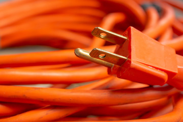 A closeup view of a male end plug of a coiled orange extension cord.