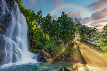 Magical waterfall with glowing sunrays and a rainbow