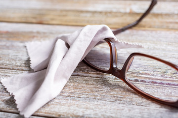 A closeup view of a pair of eyeglasses with a micro fiber cleaning cloth, on a wooden surface.