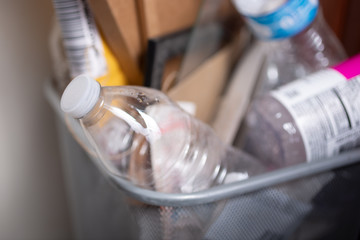 A closeup view of an unlabeled plastic water bottle, part of several pieces of trash in an overflowing trash can.