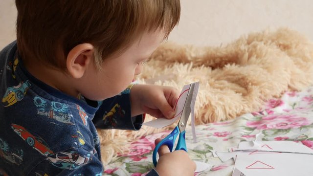 A little boy carefully cuts a paper geometric figure with scissors