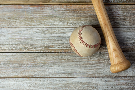 A top down view of a worn baseball and the bottom handle portion of a wooden baseball bat on a wooden surface, as a background image.