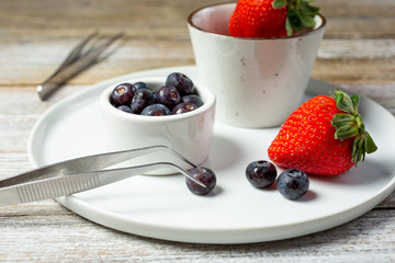 A view of a plating tweezers in a food lifestyle setup, featuring blueberries and strawberries.
