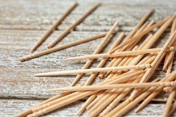 A closeup view of a pile of wooden toothpicks, on a wood table surface.