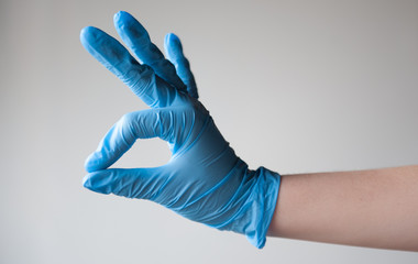 A woman's hand in a blue disposable rubber glove makes the OK sign. on light background. Pandemic, protection, infection, coronavirus