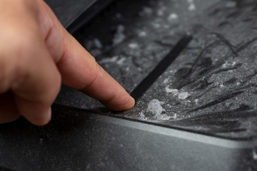 A closeup view of a finger wiping dust and dust bunnies off an electric device surface.