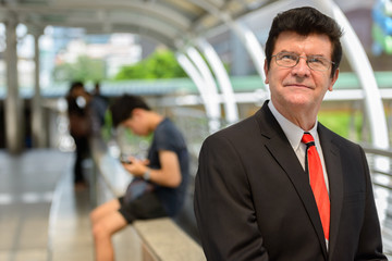 Mature handsome businessman thinking on train station at Bangkok city