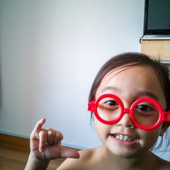 Happy toddler girl playing with red fake sunglasses at home.