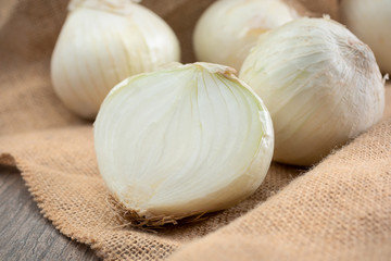 A view of several white onions, with one onion cut in half showing the inside, in a still life setting.