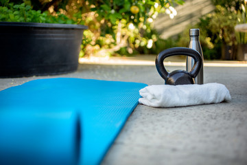 A view of fitness equipment in a backyard garden setting, featuring a yoga mat and kettlebell.
