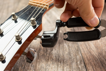 A view of a hand using a guitar string winder tool on an acoustic guitar.