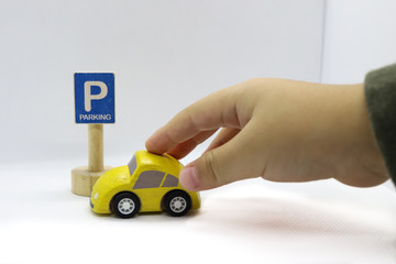 Fototapeta premium Close up of hand of a little kid pushing a yellow wooden toy car to a wooden toy parking sign on the white background