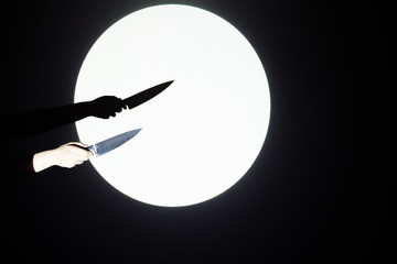 Fototapeta premium A white hand holds a huge butcher knife in its hand. The background shows a large white circle resembling the moon and black space. In the white circle there is a strong hand with a knife.