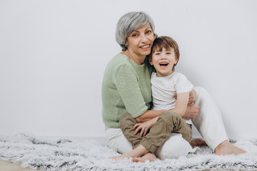 A little boy and his grandmother are having fun together against a light background