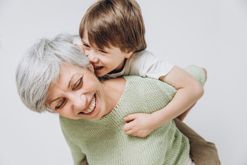 A little boy and his grandmother are having fun together against a light background