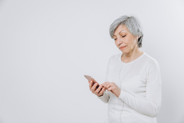 Elderly woman uses a mobile phone with hands free set, against a light background