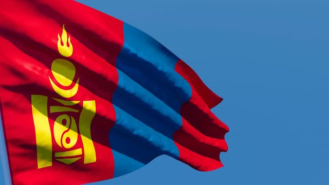 The national flag of Mongolia flutters in the wind against a blue sky