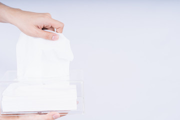 Delicate male hands pulling a white tissue paper out of a transparent crystal tissue box.