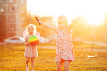 
two sisters play on the playground with a ball and a skipping rope at sunset at golden hour. Low key photo